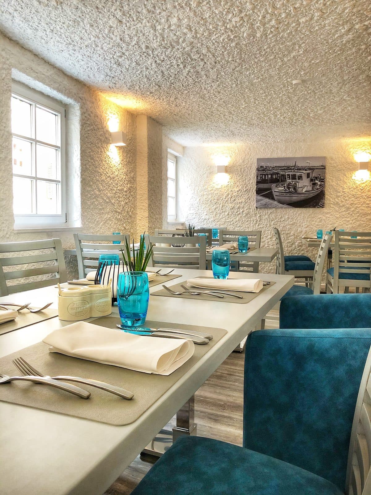 Back dining room with laid tables, blue glasses and armchairs
